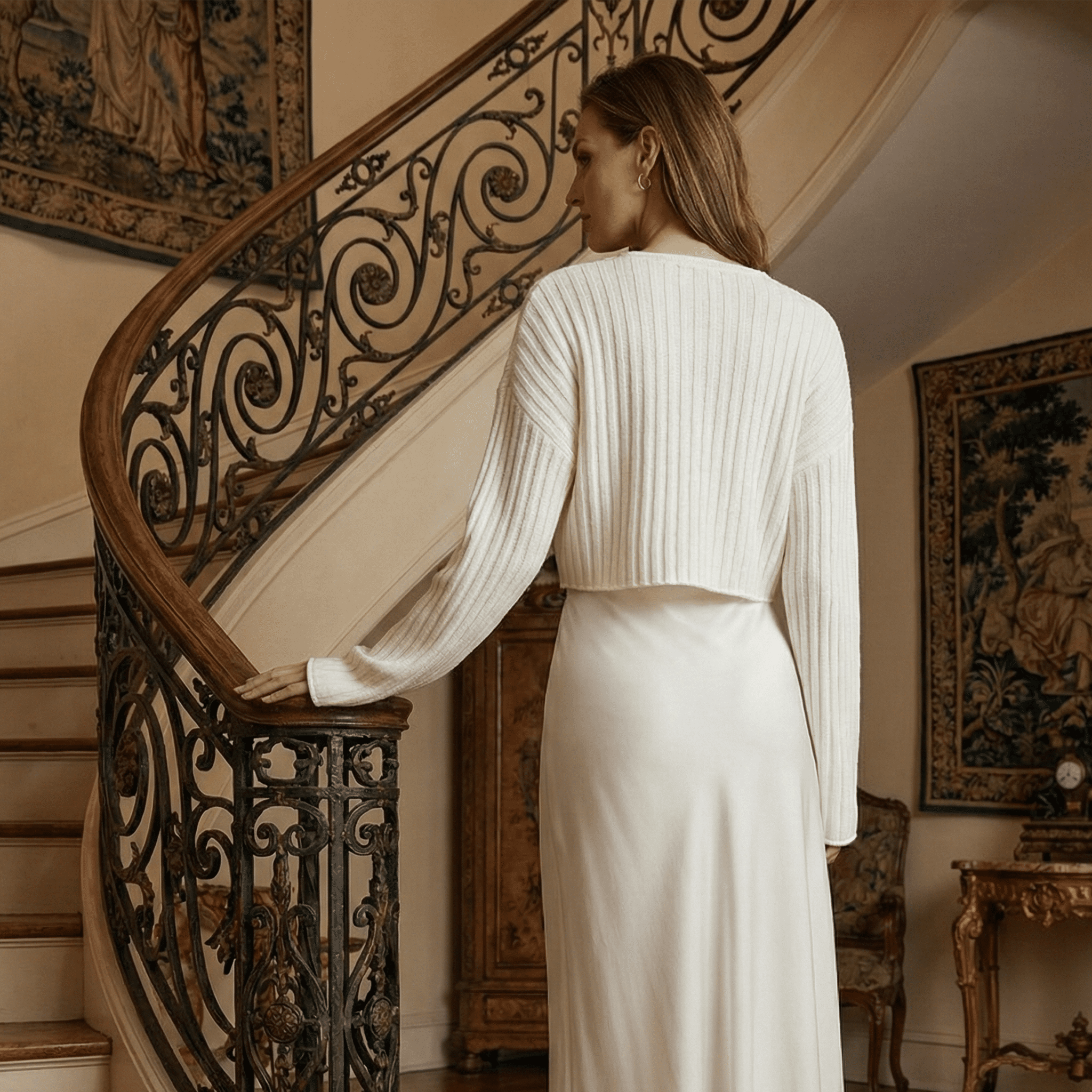 Woman in a white outfit standing on a staircase in an elegant interior setting
