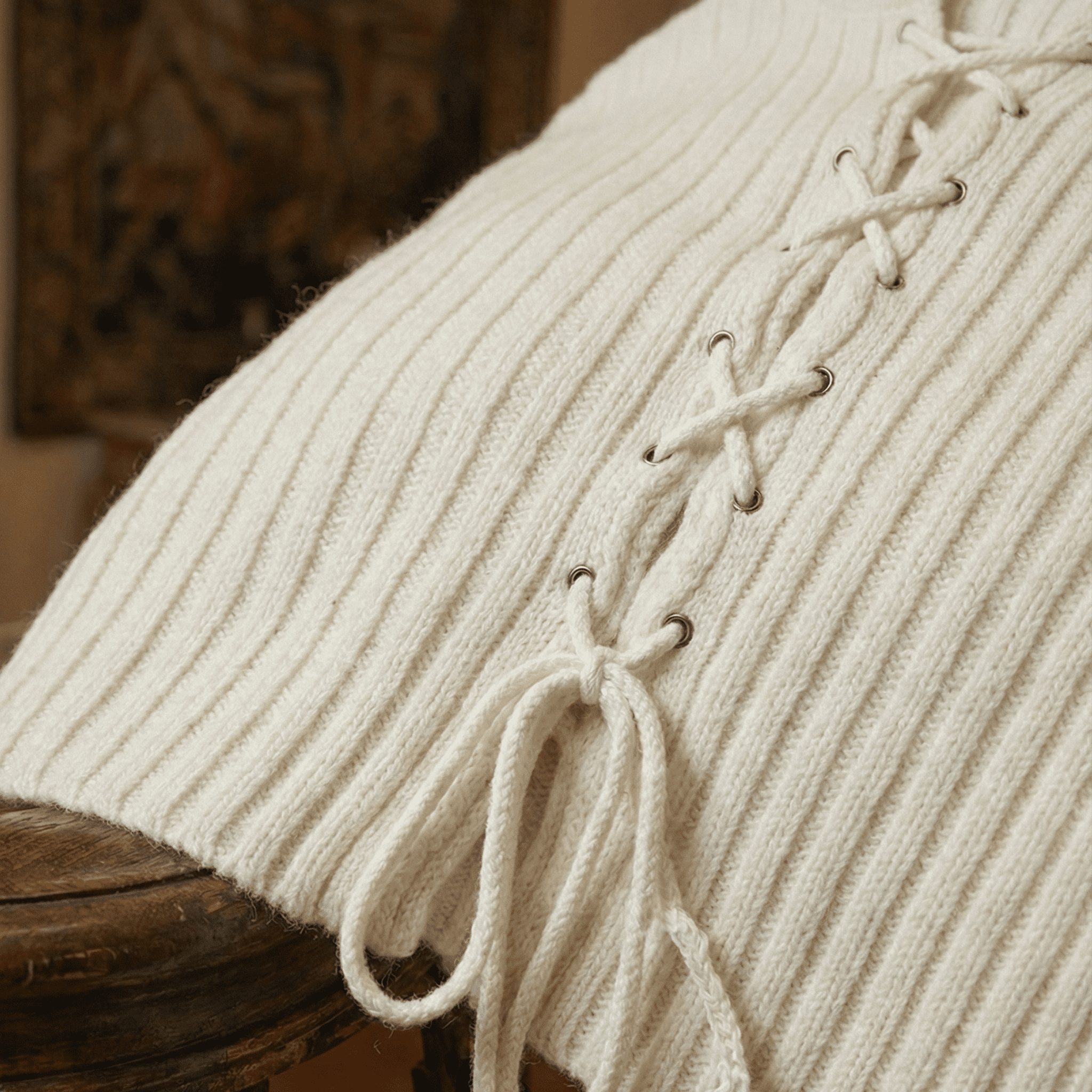 Close-up of a beige ribbed sweater with lace-up details on a wooden surface.