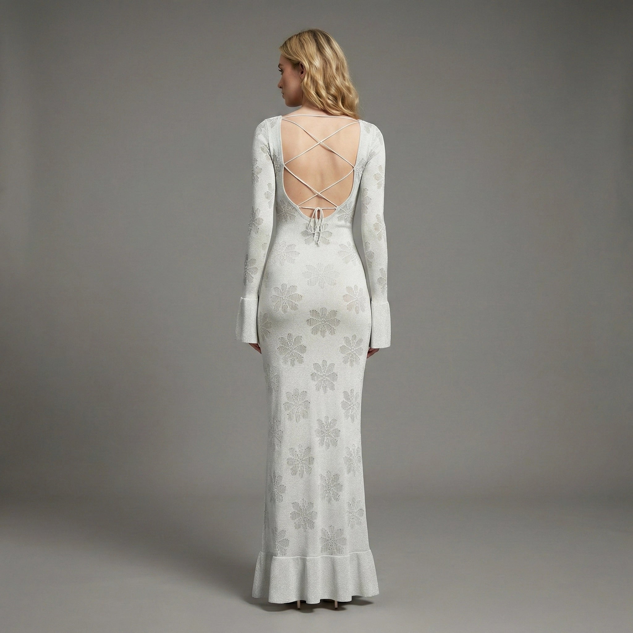 Woman wearing a long, light-colored dress with floral patterns against a gray background