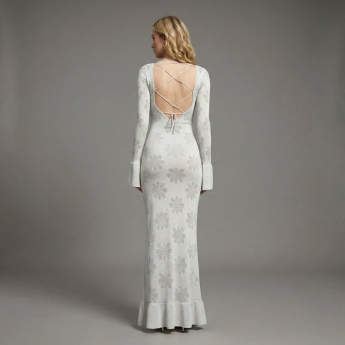 Woman wearing a long, light-colored dress with floral patterns against a gray background