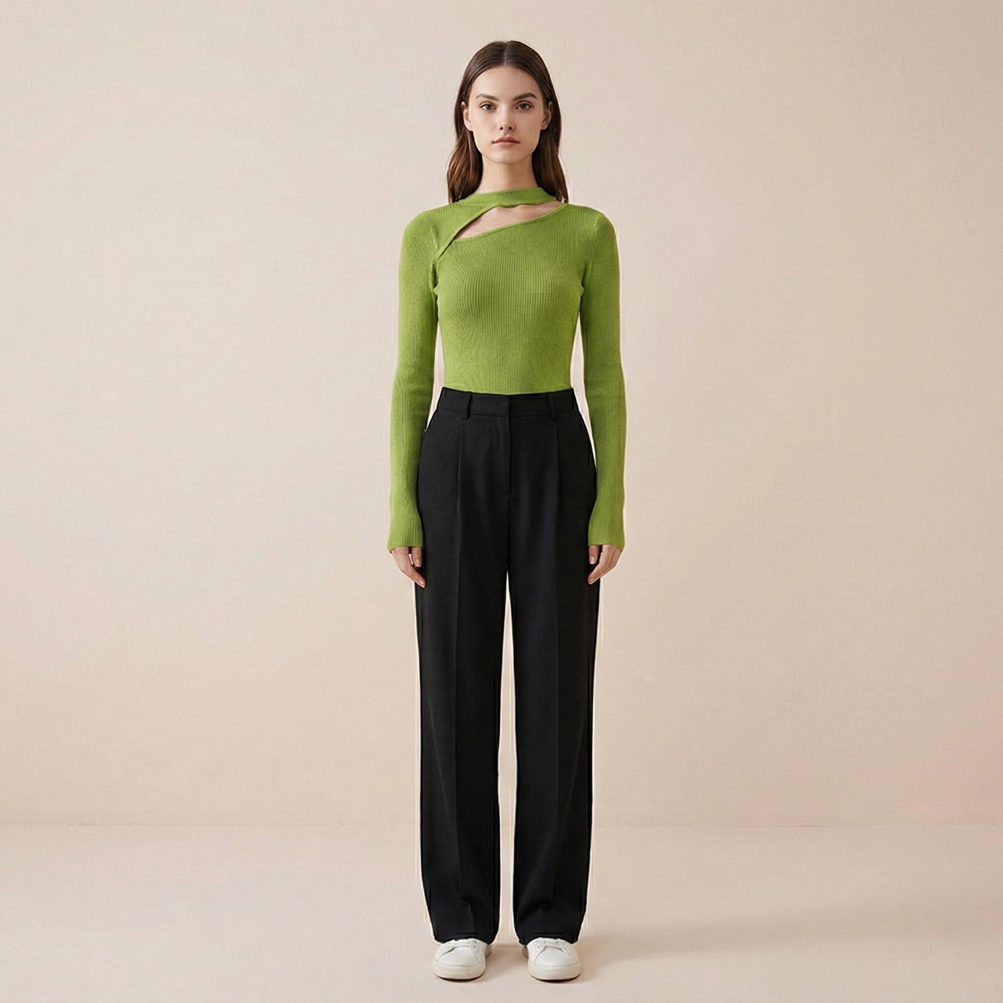 Woman wearing a green sweater and black pants on a beige background