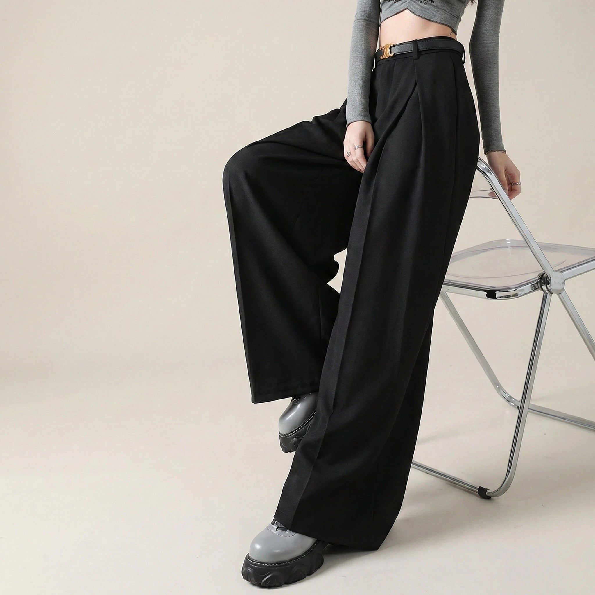 Person wearing black wide-leg pants sitting on a chair against a beige background