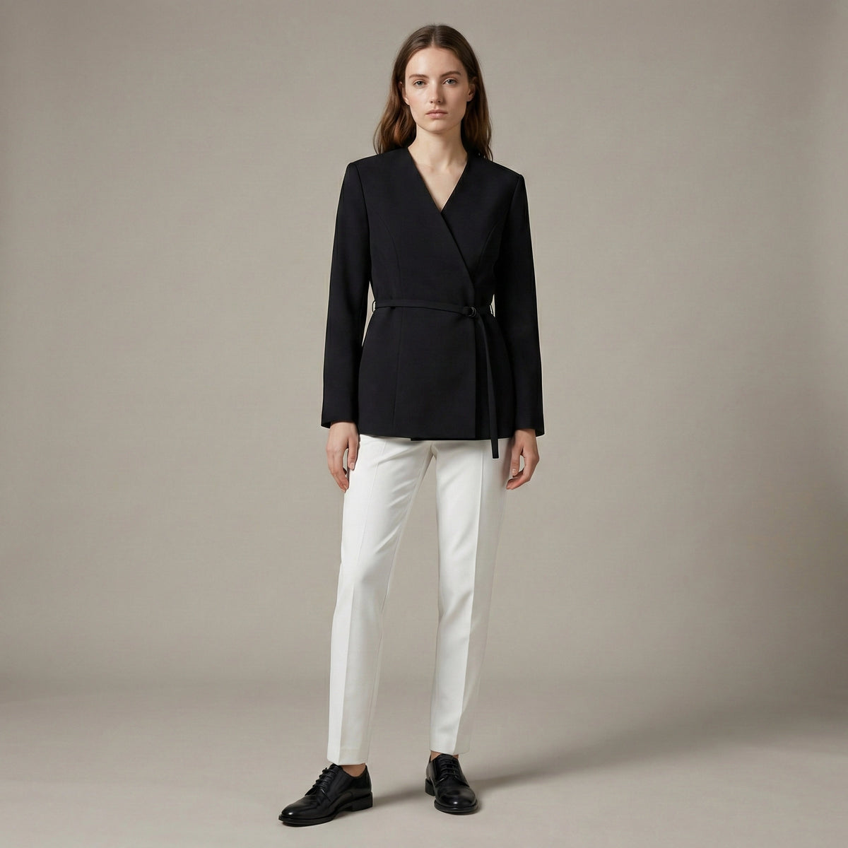Woman wearing a black blazer and white pants on a beige background
