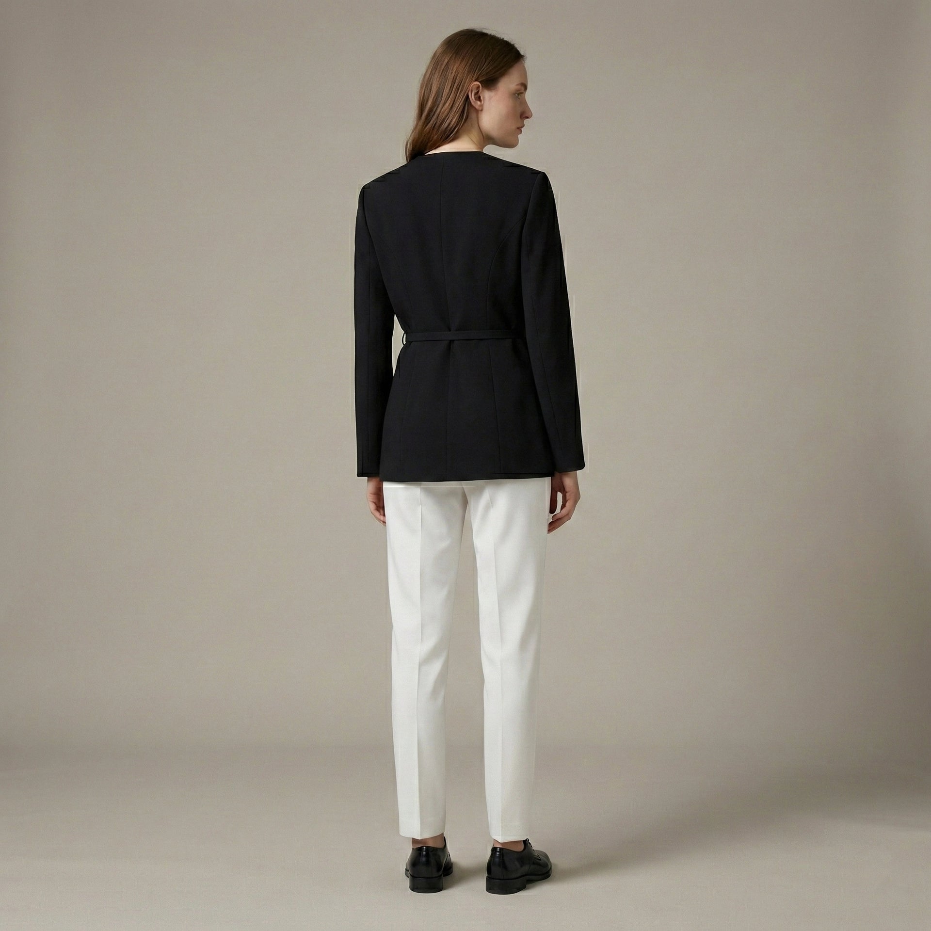 Person wearing a black blazer and white pants on a beige background