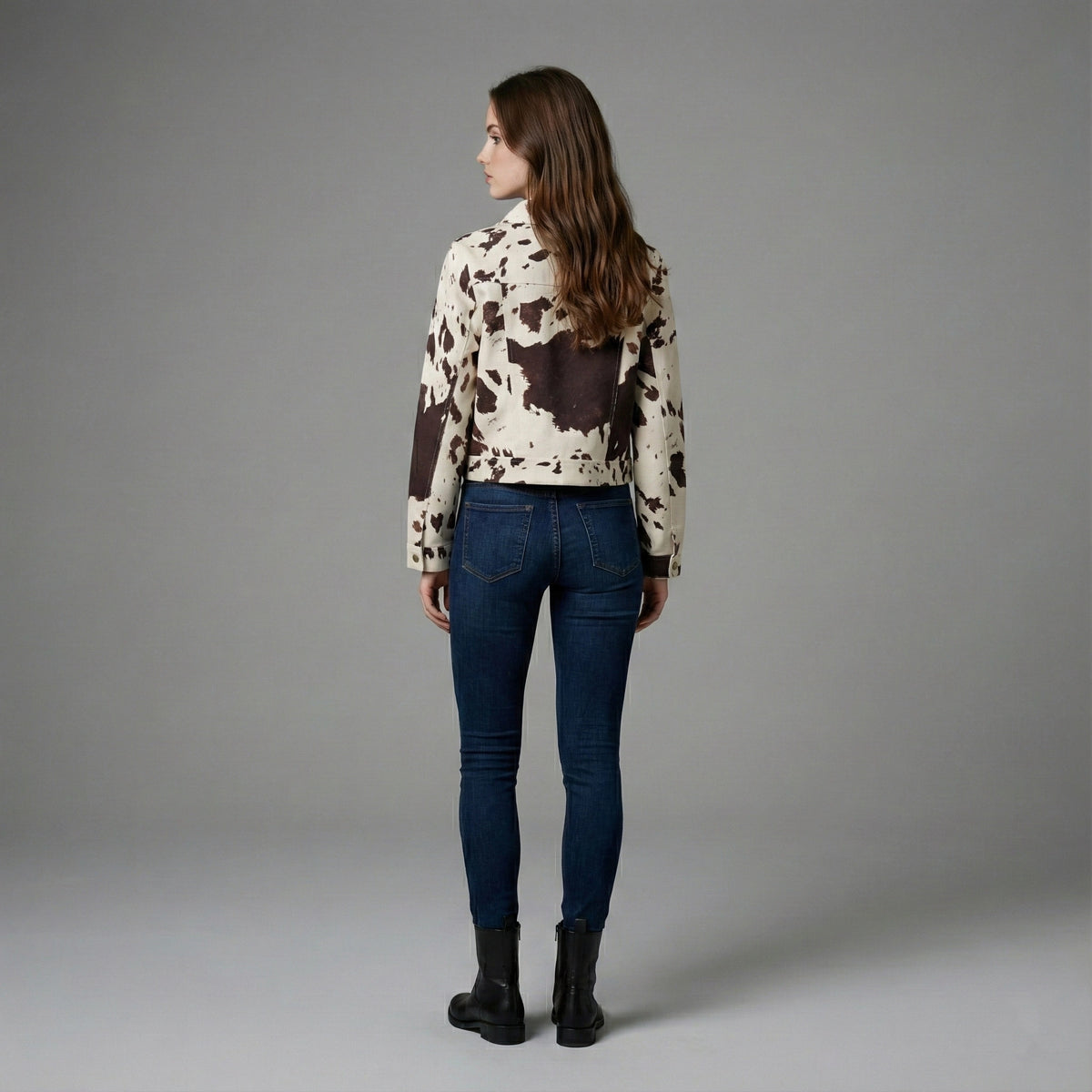 Woman wearing a cow print jacket and blue jeans on a gray background