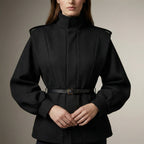 Person wearing a black coat with a belt on a neutral background