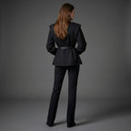 Person wearing a black suit standing against a gray background