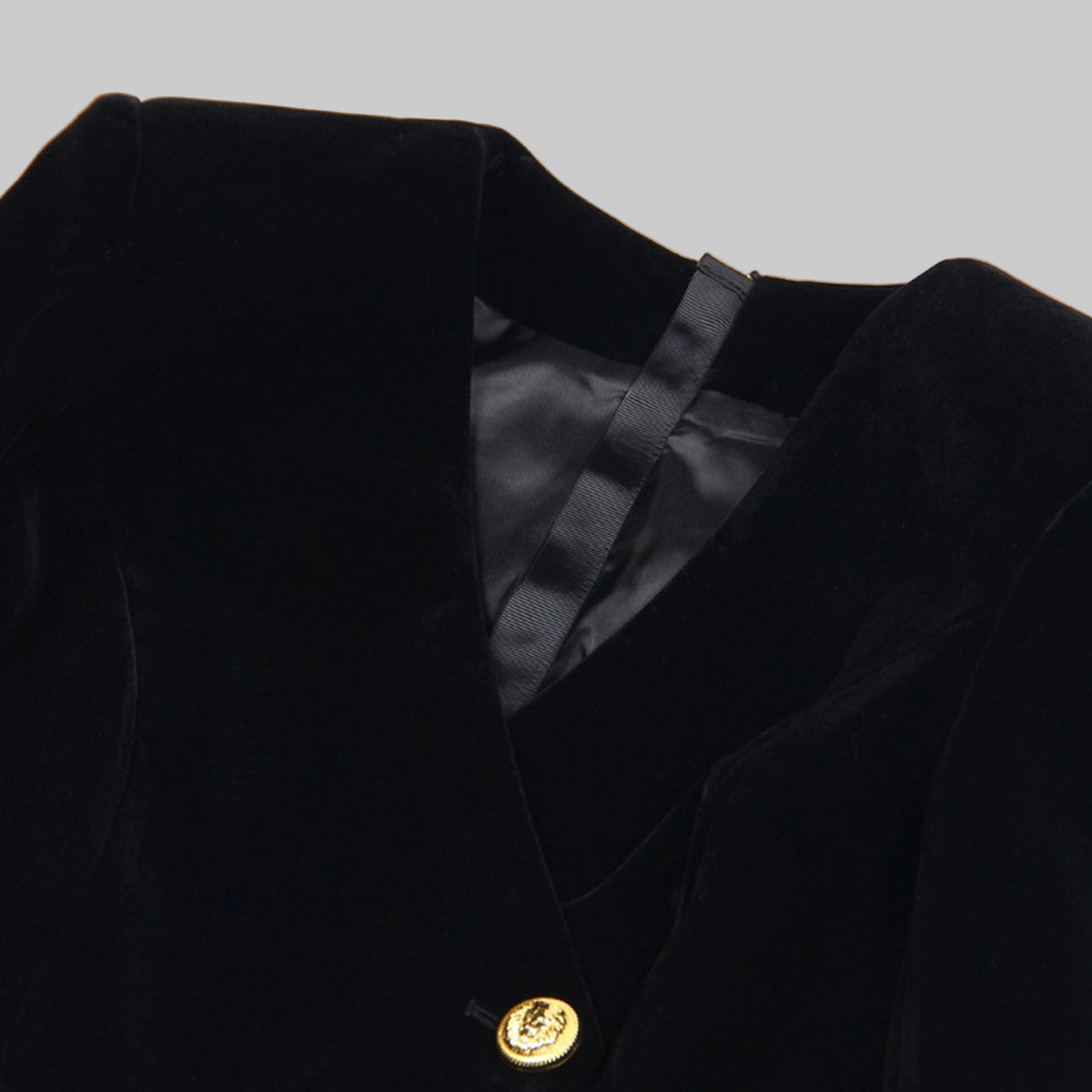 Close-up of a black blazer with a gold button on a white background