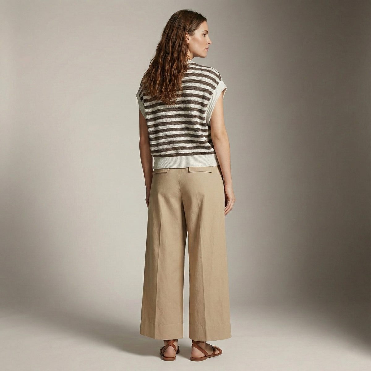 Woman wearing a striped sleeveless top and beige pants against a neutral background
