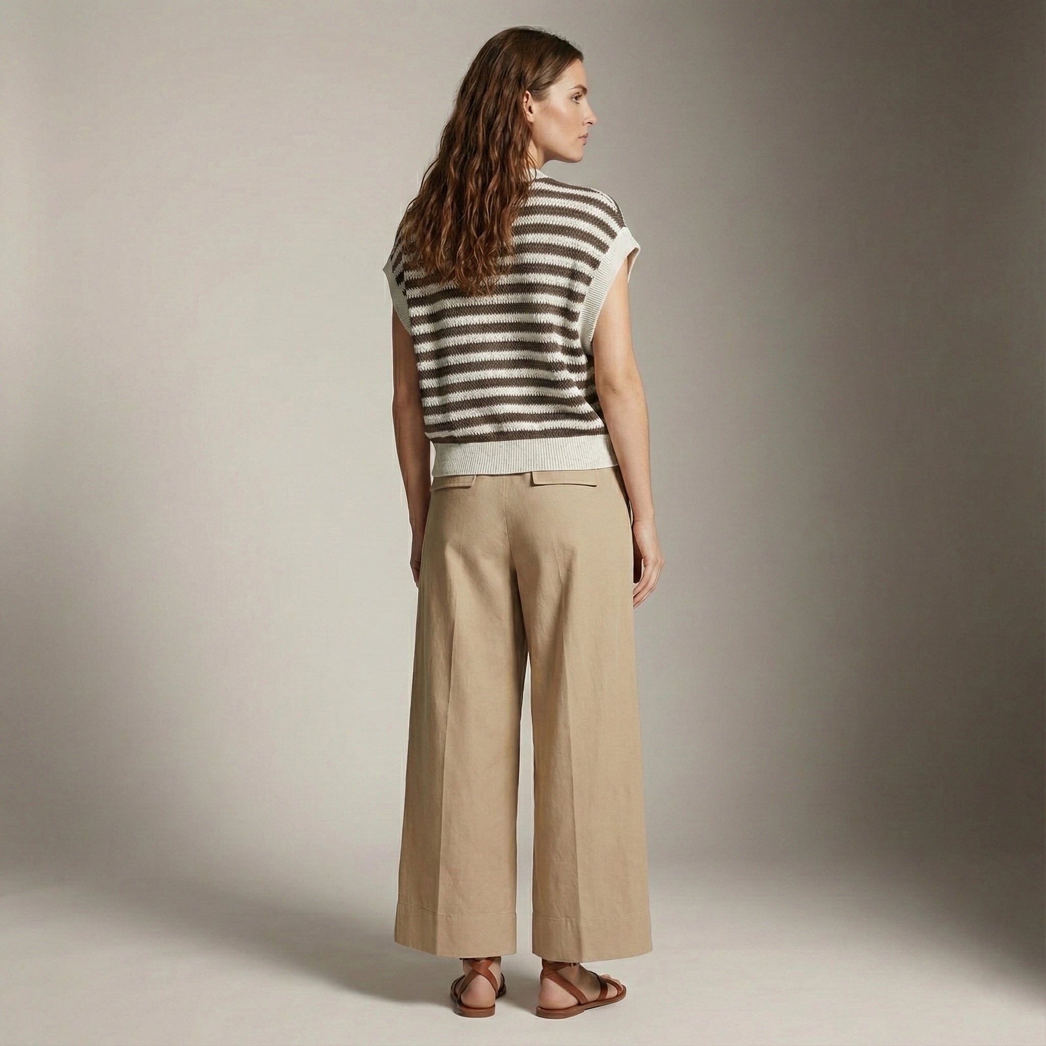 Woman wearing a striped sleeveless top and beige pants against a neutral background