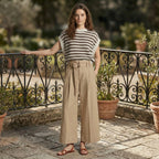 Woman standing on a stone patio with potted plants and an iron railing.