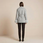 Woman wearing a light gray coat with fur cuffs and collar on a beige background