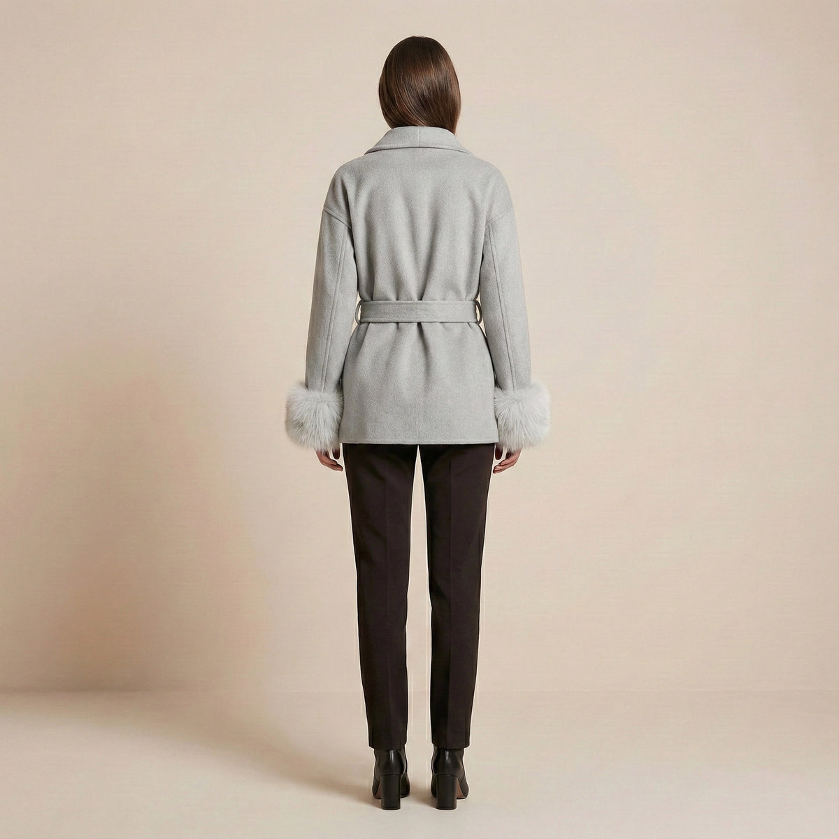 Woman wearing a light gray coat with fur cuffs and collar on a beige background