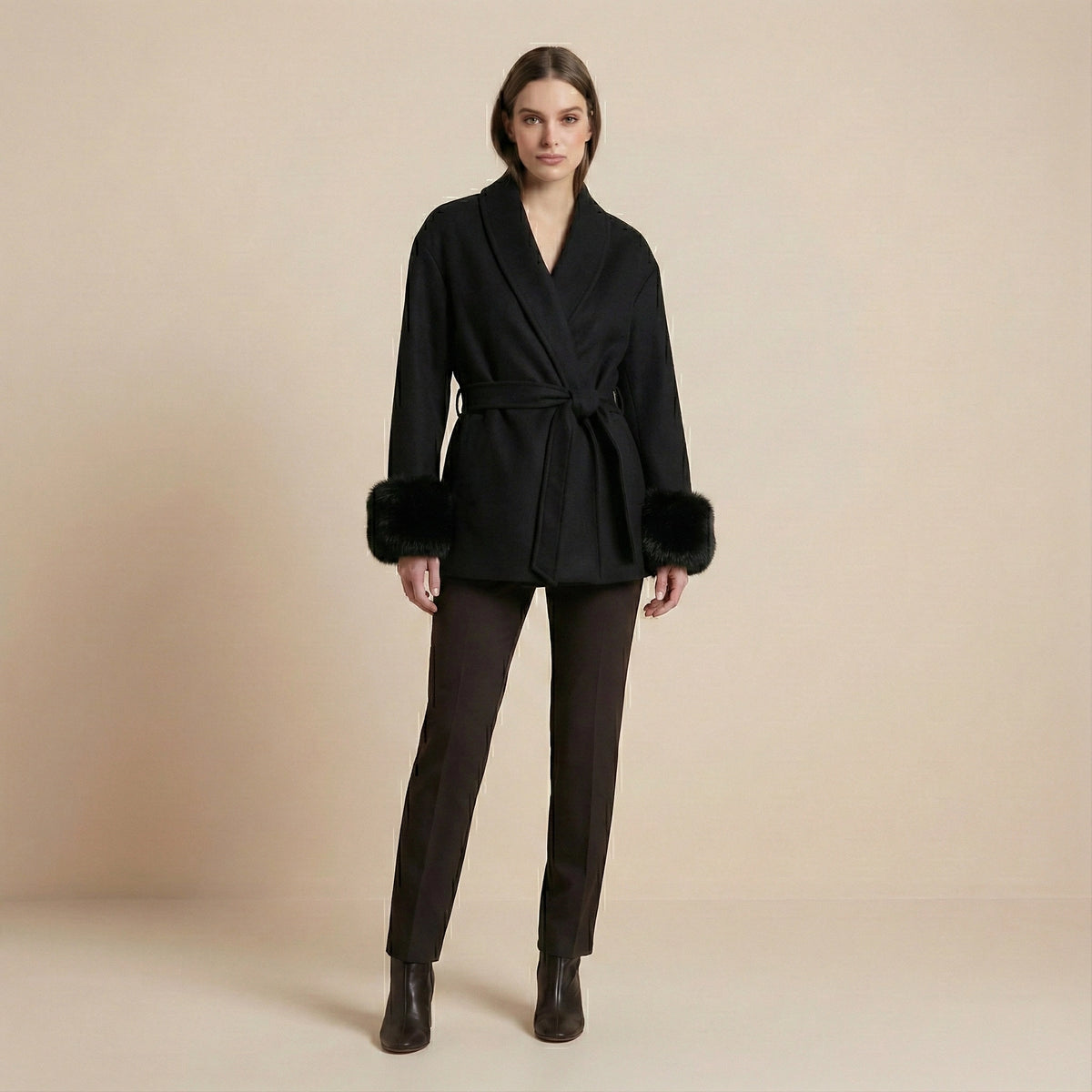 Woman wearing a black coat with fur trim on a beige background