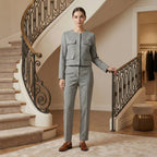 Woman in a gray suit standing in a stylish interior setting with a staircase.
