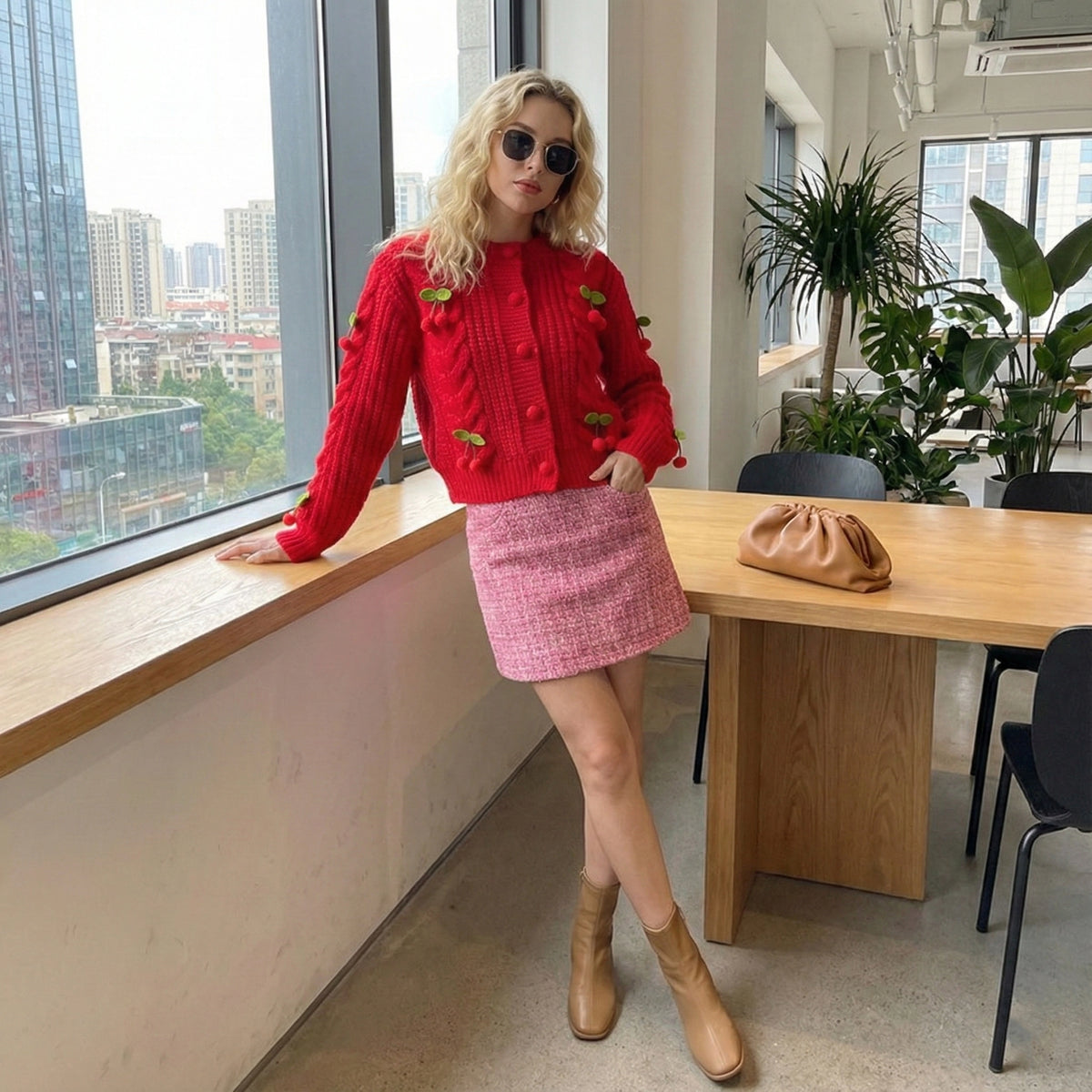 Woman in a red sweater and pink skirt standing in an office with large windows.
