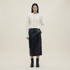 Woman wearing a white textured cardigan, black leather skirt, and black boots on a beige background
