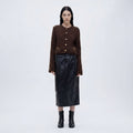 Woman wearing a brown knitted cardigan, black leather skirt, and black boots on a white background