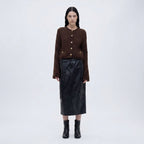 Woman wearing a brown knitted cardigan, black leather skirt, and black boots on a white background