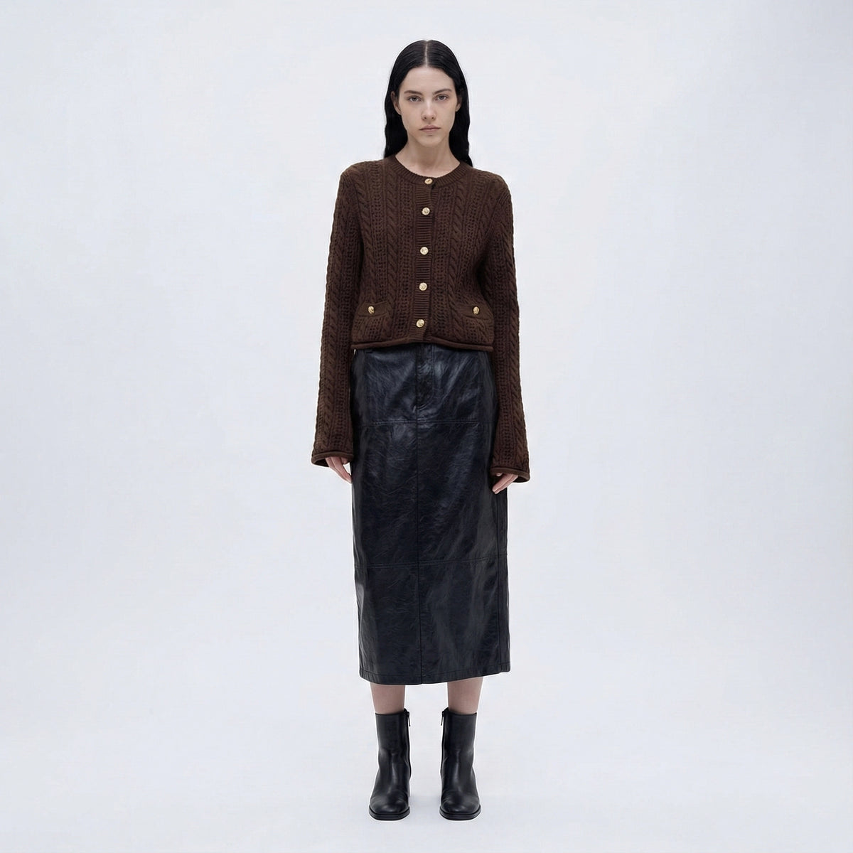 Woman wearing a brown knitted cardigan, black leather skirt, and black boots on a white background