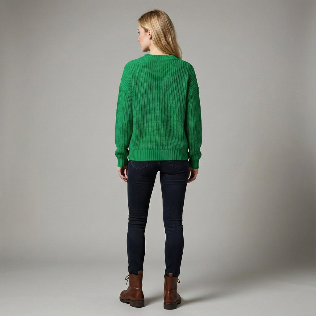 Person wearing a green sweater and dark pants on a gray background