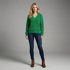 Woman wearing a green sweater, blue jeans, and brown boots on a gray background