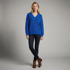 Woman wearing a blue sweater and dark jeans against a gray background