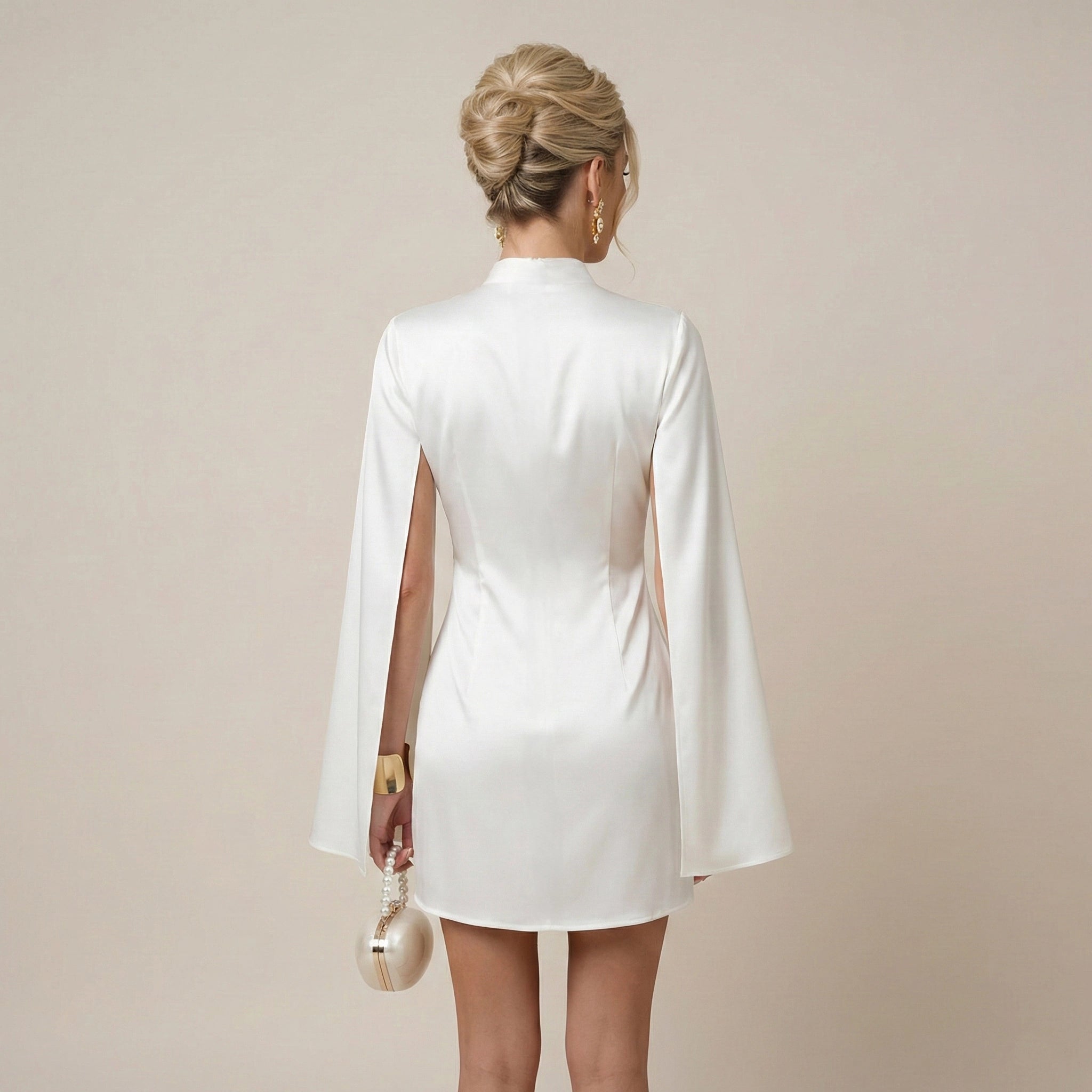 Woman wearing a white dress with cape sleeves against a beige background