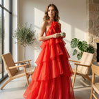 Woman in a red dress holding a cup in a sunlit room with plants and chairs.
