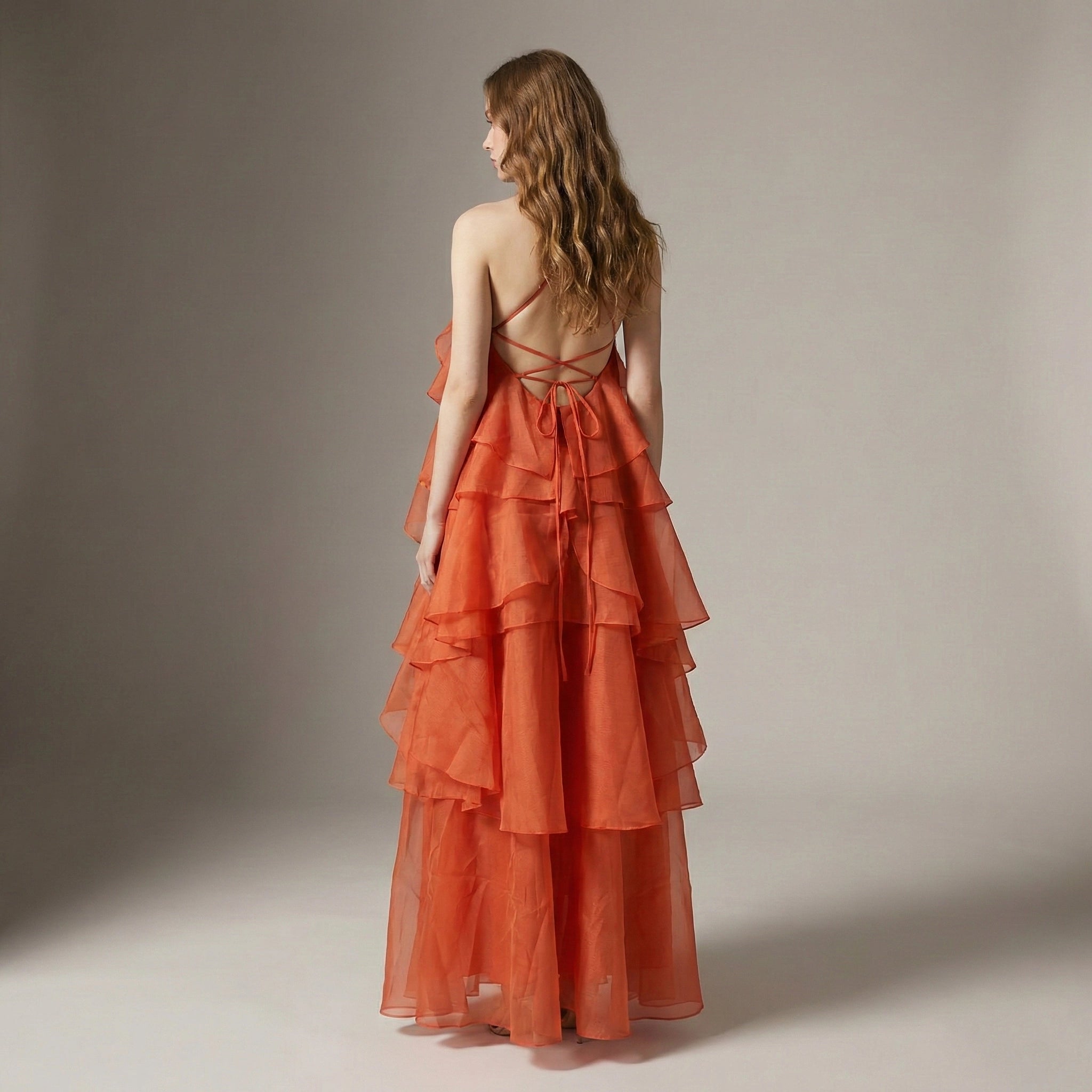 Woman wearing an orange tiered dress with a backless design on a neutral background
