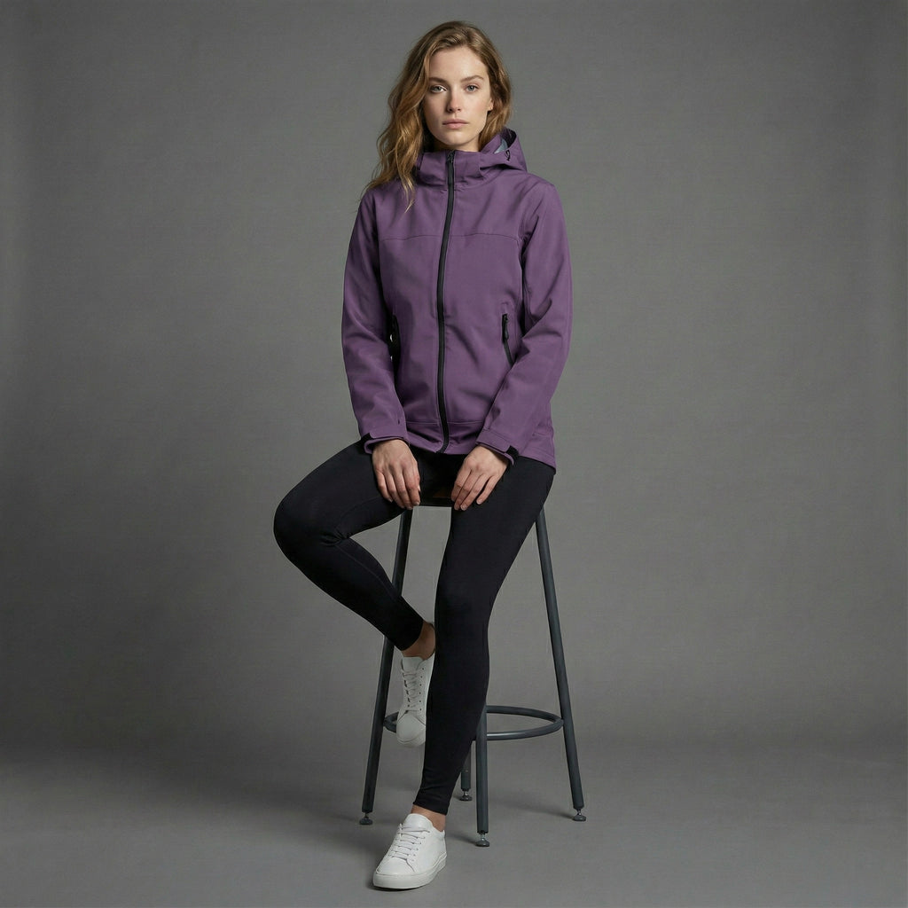 Woman wearing a purple jacket sitting on a stool against a gray background