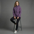 Woman wearing a purple jacket sitting on a stool against a gray background