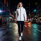Woman in a white jacket walking on a city street at night.
