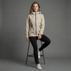Woman wearing a beige jacket sitting on a stool against a gray background