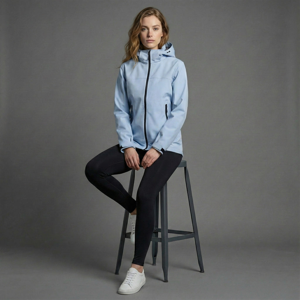 Woman wearing a light blue jacket sitting on a stool against a gray background