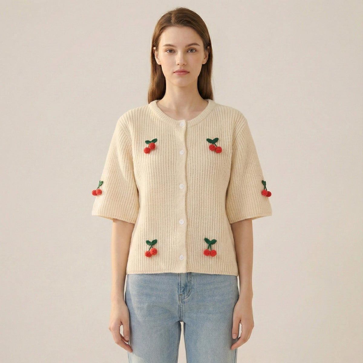 Woman wearing a beige cardigan with cherry embroidery on a plain background