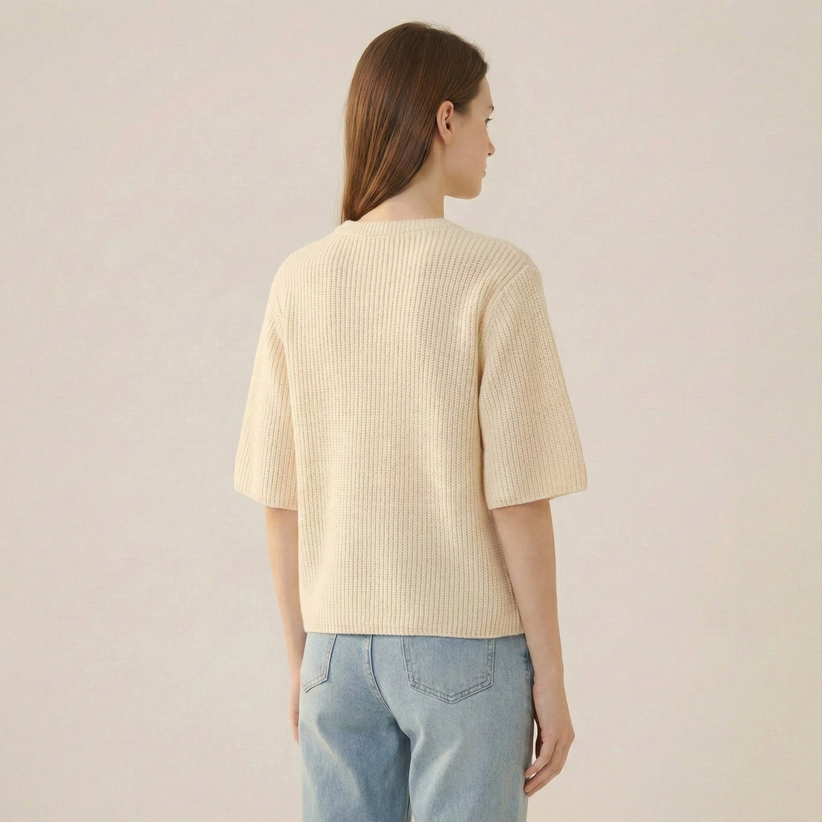 Person wearing a light yellow ribbed sweater and light blue jeans on a plain background