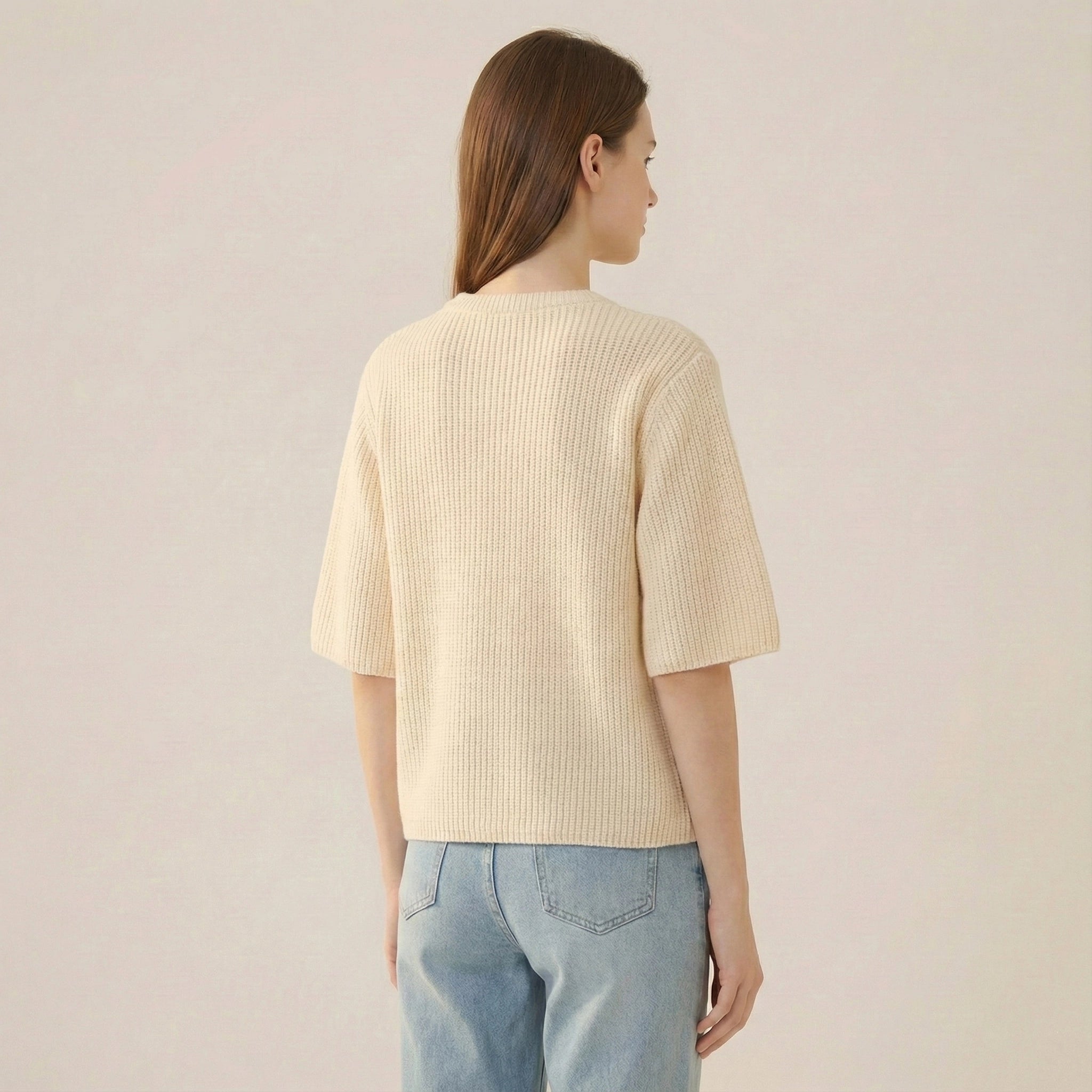 Person wearing a light yellow ribbed sweater and light blue jeans on a plain background
