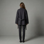 Person wearing a dark gray coat and pants against a plain background