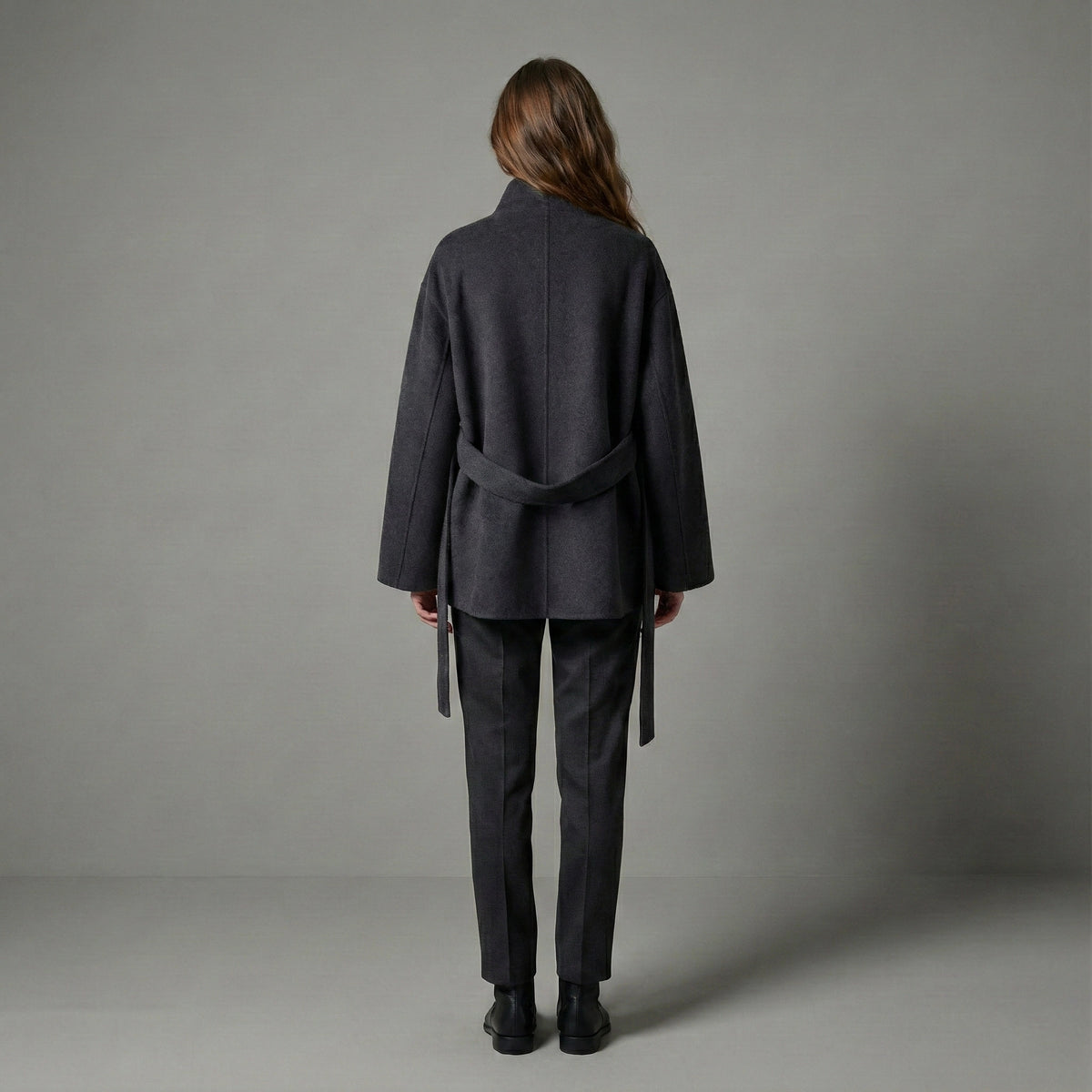 Person wearing a dark gray coat and pants against a plain background