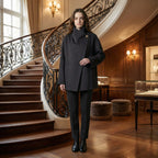 Woman in a black coat standing in an elegant interior setting with a staircase.