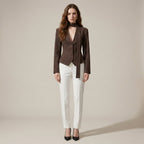Woman wearing a brown blazer over a black top with white pants on a beige background