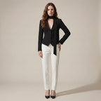 Woman wearing a black blazer and white pants against a beige background