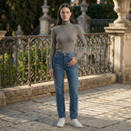 Woman wearing a gray turtleneck and blue jeans standing on a stone path with decorative railings.