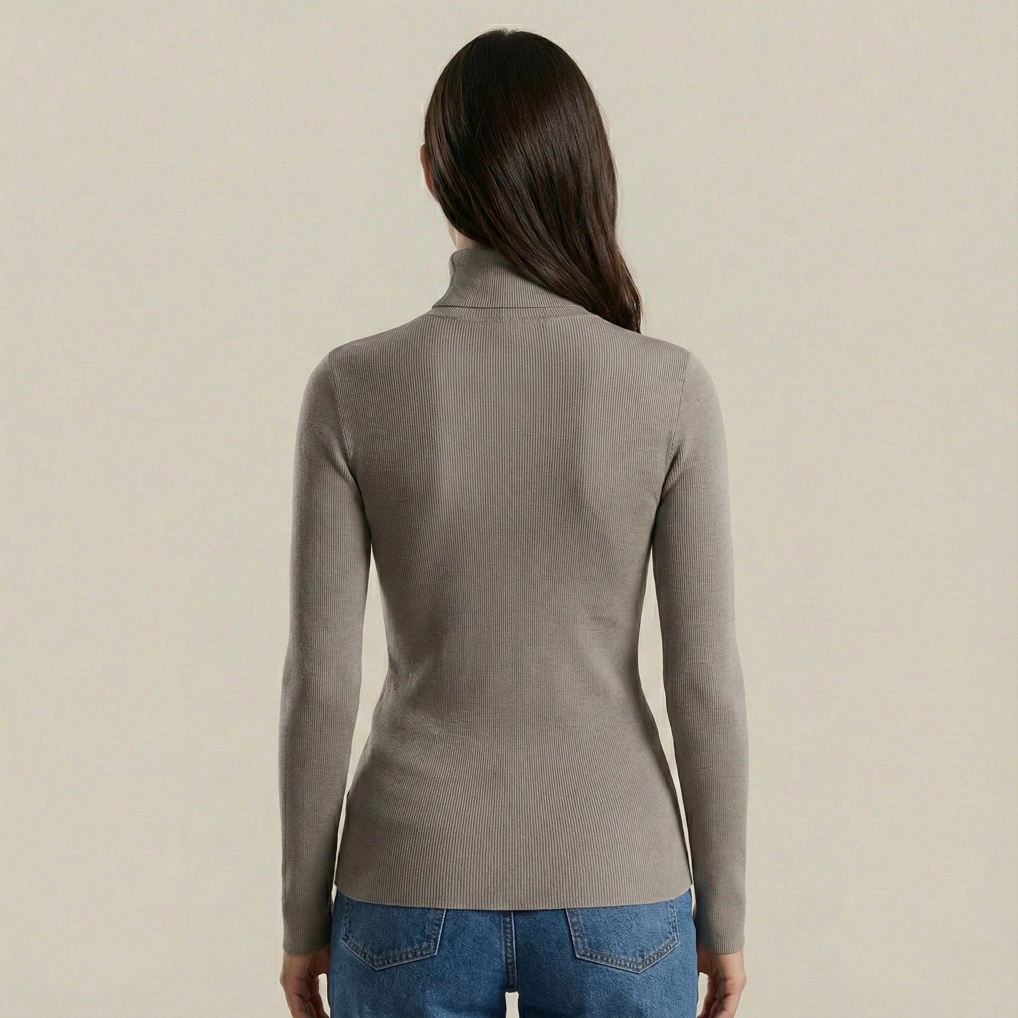 Woman wearing a gray turtleneck sweater and blue jeans on a beige background