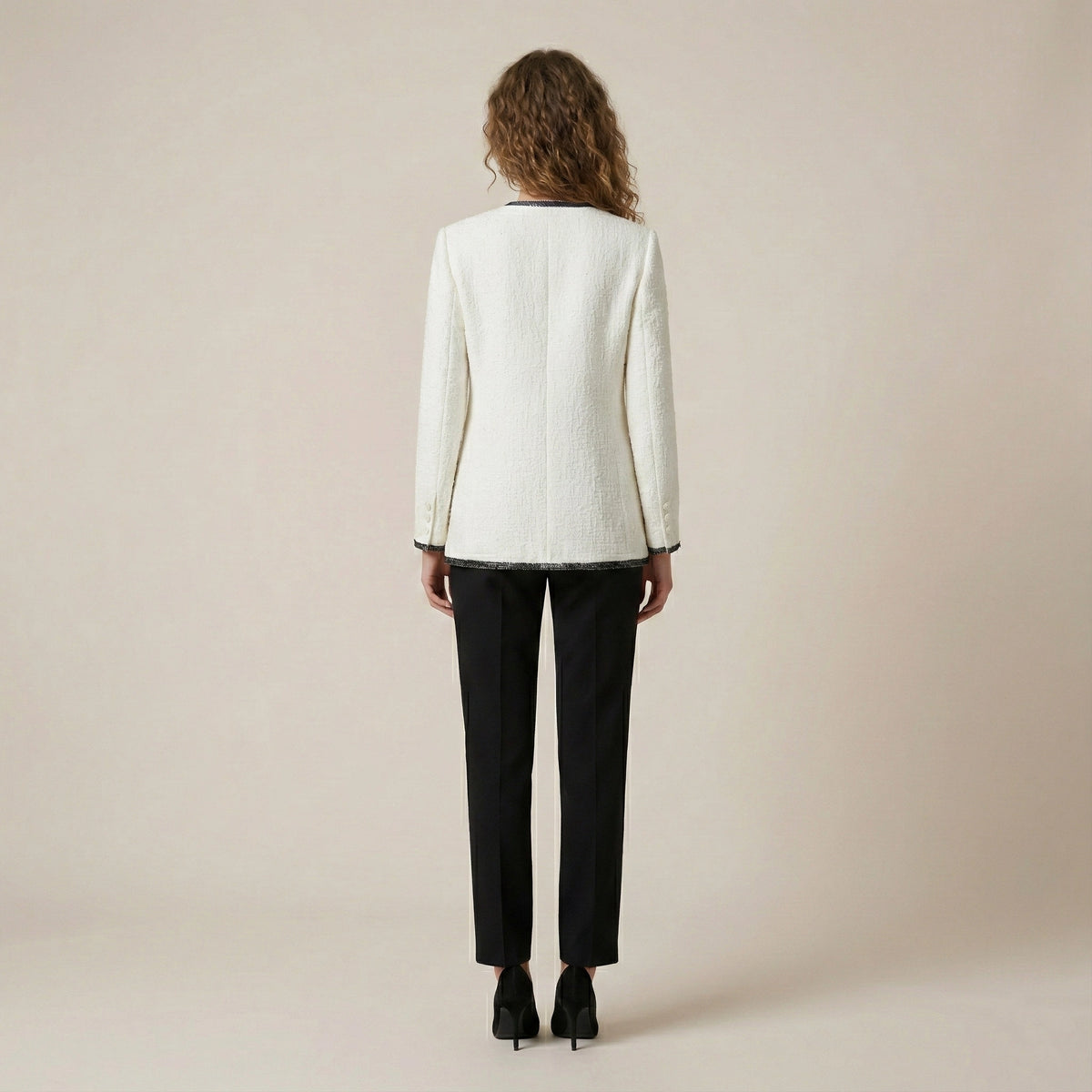 Person wearing a white blazer and black pants on a beige background