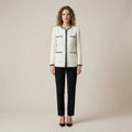 Woman wearing a white jacket with black accents and black pants on a beige background
