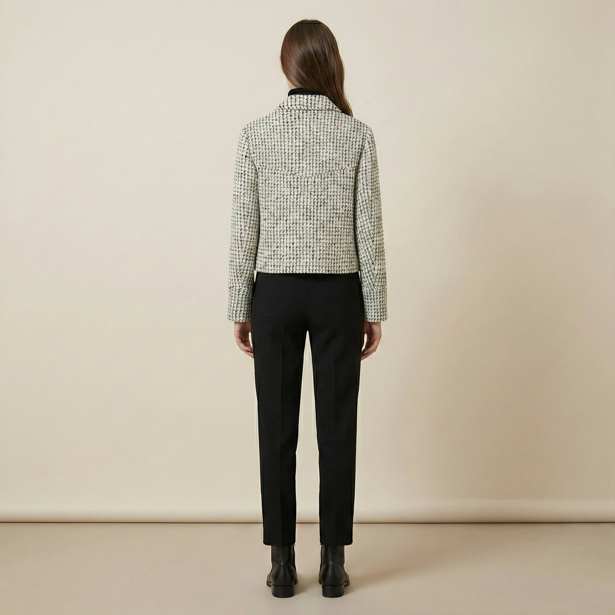 Person wearing a checkered shirt and black pants against a beige background