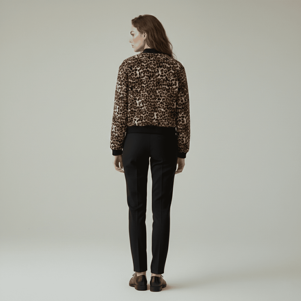 Person wearing a leopard print jacket and black pants on a plain background