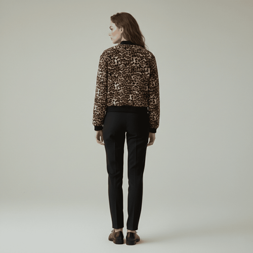 Person wearing a leopard print jacket and black pants on a plain background